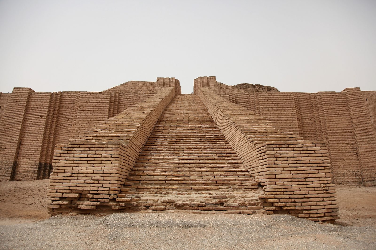 The Great Ziggurat of Ur, looking straight up the central staircase, built about 2100 BC. Three stairways of about a hundred steps each meet at a gate on the first terrace; behind them the platform is a solid mountain of some seven million sun-dried bricks under a skin of baked brick. On a floodplain with no stone and no timber, this is what mud can do when a king can command the labor of a whole city. The lower facing and this stair were rebuilt on the ancient core in the 1980s; the mass behind them is the original.