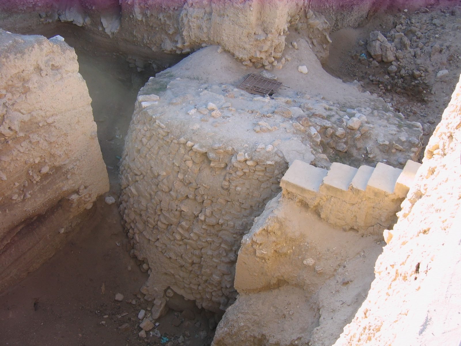 The stone tower of Jericho at Tell es-Sultan, near the Jordan River, seen from above in its excavation trench. Built about 8000 BC — before a single brick was laid in Mesopotamia — it stands about 28 feet, five men on each other's shoulders, with a staircase inside. This plate is dated five thousand years before the rest of the lesson on purpose: it is the near-miss. A wall, a tower, maybe two thousand people. Ask three questions — could one farmer feed anyone but his own family, did anyone have a job besides growing food, could anyone prove what he owned — and Jericho fails all three. Town, not city.