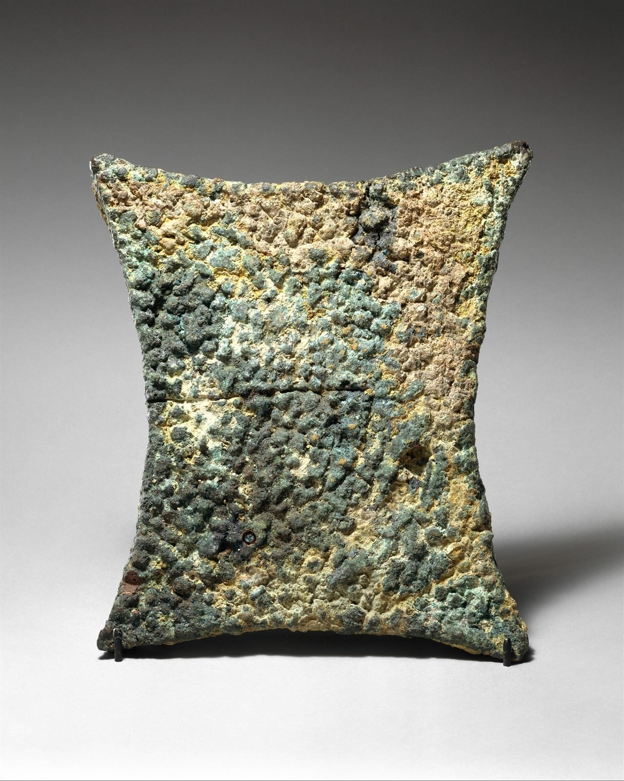 Copper cast in the shape of a stretched animal hide, with four corners a porter could grip. Ingots of this shape crossed the whole Bronze Age sea. The Uluburun hold carried 354 of them — ten tons of copper, about the weight of an empty school bus.